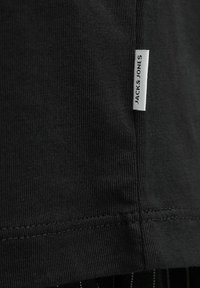 Schwarzes, geripptes T-Shirt aus Stoff mit einem Seitenschild, auf dem "JACK & JONES" steht. Es hat ein einfaches, tailliertes Design und saubere Nähte.