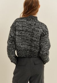 Kort svart och grå stickad tröja med hög halsringning, texturerad tyg och ribbad nederkant, i kombination med mörka skräddarsydda byxor.