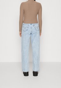 Light blue, loose-fitting jeans with a high waist and embroidered back pockets; paired with a fitted brown ribbed top. Black chunky shoes.