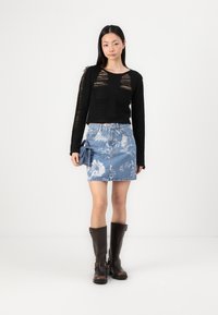 Črna dolga majica z vodoravnimi jermeni, denimska mini krila s cvetličnim tiskom in rjavi usnjeni škornji do kolen z zaponkami.