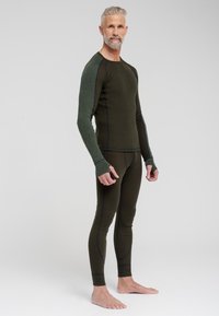 Olivenfarvet termotop og -bukser lavet af blødt materiale. Langærmerne har teksturerede grønne detaljer og tommelfingerhuller. Flade sømme er synlige.
