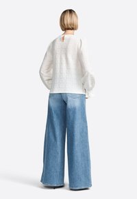 Blouse blanche texturée avec des manches bouffantes et un dos en œil de perdrix, associée à un jean en denim bleu délavé à jambes larges.