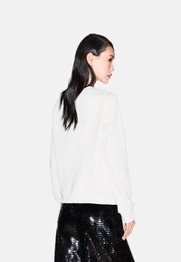 Sudadera blanca con un escote redondo y puños acanalados, combinada con una falda brillante de lentejuelas negras, vista desde la parte posterior.