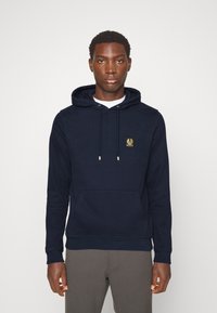 Tumši zilas krāsas kapuciņa, izgatavota no mīksta auduma, ar kangaroo kabatu, regulējamām auklām un mazu zeltītu logo uz krūtīm.