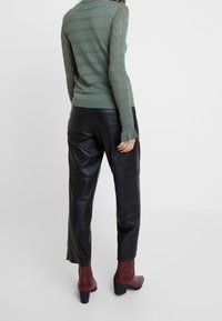 Zelený pletený svetr s texturovaným vzorem; černé kožené kalhoty; víno barevné kotníkové boty s blokovým podpatkem.