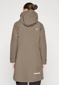 Pruun veekindel jakk kapuutsiga, sirge lõikega, pikkade varrukatega ja valge logoga detailiga. Omadustega reguleeritavad varrukaotsad ja helkurelement.