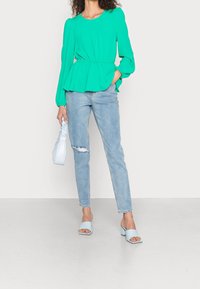 Top peplum a maniche lunghe teal con vita elasticizzata, jeans strappati azzurri, mule con tacco blocco azzurri e borsa azzurra arricciata.