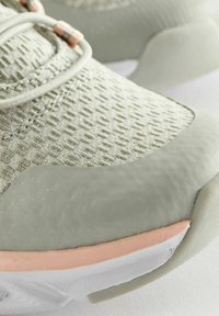 Světle zelená sportovní bota s mřížkovou tkaninou, hladkou gumovou podrážkou a broskvovou akcentací. Obsahuje texturovaný vzor a zesílenou špičku.