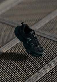 Zwarte sneaker met meshpanelen, gegoten rubberen zool en textuuraccenten. Bevat veters en een trekhaak op de hiel.