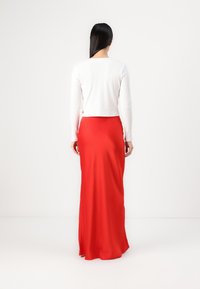 Hvit ribbet langermet topp sammen med en flytende rød sateng maksimal skirt, som viser myk tekstur og en elegant silhuett.