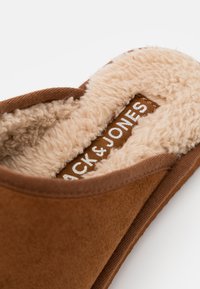 Brune tøffel med myk faux pelsfôr, med en glatt overflate og et merke med "Jack & Jones." Designet er enkelt og behagelig.