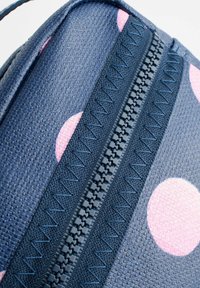 Jūras zilas krāsas soma ar rozā punktiņiem un strukturētu virsmu. Tai ir centrāla rāvējslēdzēja ar saskaņotu jūras zilu krāsu, izrotāta ar zigzaga šuvēm.