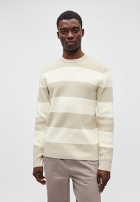 Beige- und cremefarbener, gestreifter Pullover mit gerippter Textur, Rundhalsausschnitt und langen Ärmeln, kombiniert mit hellen Hosen.