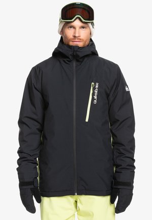 Schwarze wasserdichte Jacke mit hohem Kragen, Frontreißverschluss und kontrastierenden gelben Akzenten. Enthält Handschuhe und Schneebrille, was einen geschichteten Look ergibt.
