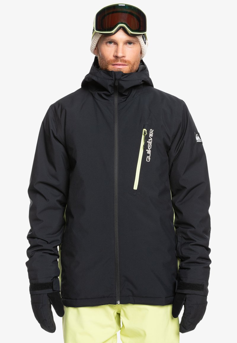 Schwarze wasserdichte Jacke mit hohem Kragen, Frontreißverschluss und kontrastierenden gelben Akzenten. Enthält Handschuhe und Schneebrille, was einen geschichteten Look ergibt.