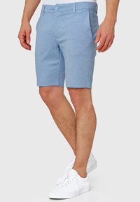 Lyseblå shorts lavet af et tekstureret stof, med knaplukning, sidelommer og et slankt design. Kombineret med hvide sneakers.