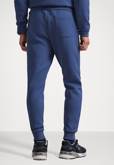 Γαλάζιο βαμβακερό παντελόνι jogger με στενή εφαρμογή, διαθέτοντας πίσω τσέπη και ριμπ μανσέτες. Συνδυάζεται με σκούρα αθλητικά παπούτσια.