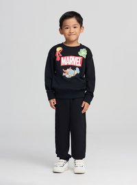 Felpa nera con logo "MARVEL" e grafiche di personaggi, abbinata a pantaloni della tuta neri e sneakers bianche. Tessuto liscio e vestibilità comoda.
