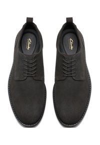Zapatos de ante gris oscuro con punta redondeada, que cuentan con seis agujeros para cordones, costuras decorativas y una suela de goma texturizada. Incluye la marca Clarks.