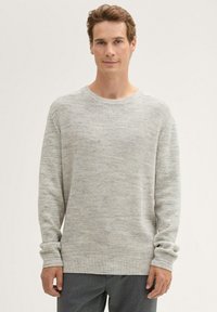 Lichtgrijze trui met een gestructureerd breipatroon, ronde halslijn en lange mouwen; gedragen met donkergrijze broek.