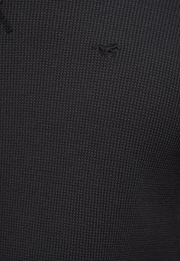 Fekete, texturált anyag kis, hímzett logóval. Az anyag rácsmintás, finom, de részletes megjelenést kölcsönözve neki.