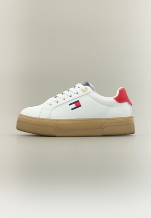 Zapatillas deportivas sintéticas blancas con suela de goma, talón en contraste rojo, detalles en azul y un pequeño logotipo con franjas rojas y azul marino.