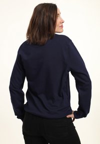 Felpa blu navy realizzata in un tessuto morbido; presenta maniche lunghe, scollatura rotonda e una vestibilità comoda. I pantaloni neri completano il look.