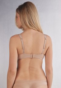 Beige bh met verstelbare banden, een haak-en-oogsluiting, een gladde stof en een minimalistisch ontwerp. De achterkant benadrukt de silhouet.