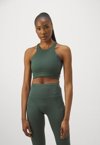 Mörkgrön sport-bh med hög halsringning, kombinerad med matchande högmidjade leggings med sidoficka och diskret logotyp.