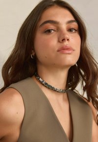 Polírozott ezüstből készült choker nyaklánc, kalapált textúrával, semleges színű ujjatlan toppal viselve, melynek mély V-kivágása van.