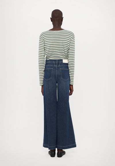 Bredde ben mørkeblå denim jeans med høy midje, kombinert med en grønn og hvitstripet langermet skjorte med rund hals.