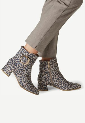Bottines à imprimé léopard, boucle dorée et fermeture éclair latérale, portées avec un pantalon court marron clair.