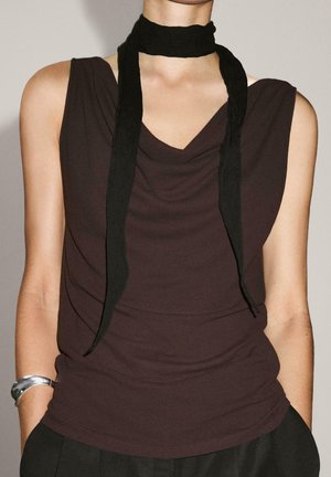 Brown sleeveless top with a draped neckline, paired with a black scarf. Smooth fabric with a fitted silhouette and a silver bracelet on the wrist.