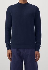 Marinblå stickad tröja med rund halsringning, ribbade ärmslut och nederkant. Texturen är slät med medelstor tjocklek, lämplig för lager-på-lager.