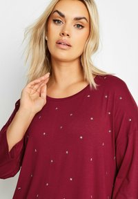 Bordeaux långärmad topp med en avslappnad passform, rund halsringning och spridda silverstjärnprydnader över framsidan. Slät tygtextur.