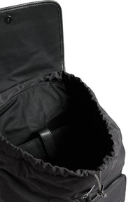 Zaino nero con scomparto principale aperto, chiusura con coulisse, flap con bottone a scatto e tasca interna visibile con cinturino in pelle.