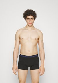 Schwarze Boxershorts mit konturiertem Schnitt, ausgestattet mit einem blauen Markenbund. Glatte Textur, minimalistisches Design und mittellange Schnitt bis zum Oberschenkel.