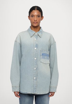 Camicia in denim blu chiaro con bottoni sulla parte anteriore, colletto a punta e taschino sul petto con la scritta "MOSCHINO JEANS" in blu. Vestibilità rilassata.