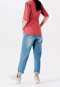 Top corallo con maniche a palloncino, cintato in vita; jeans in denim blu chiaro, loose-fit; sneakers crema con risvolti.