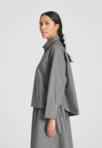Camicia grigia con bottoni, dalla vestibilità comoda, maniche lunghe e colletto. Realizzata in tessuto leggero con una texture liscia.