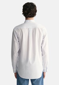 Camisa blanca de manga larga con cuello abotonado, que presenta una textura suave y un dobladillo curvado. Acentos azules en el cuello y los puños.