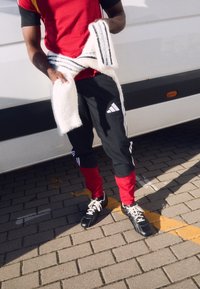 Sarkans un melns sporta krekls, melnas bikses ar sarkaniem akcentiem un baltajām svītrām, tur baltu pūkainu šalli. Melni sporta apavi ar baltiem šņorējumiem.