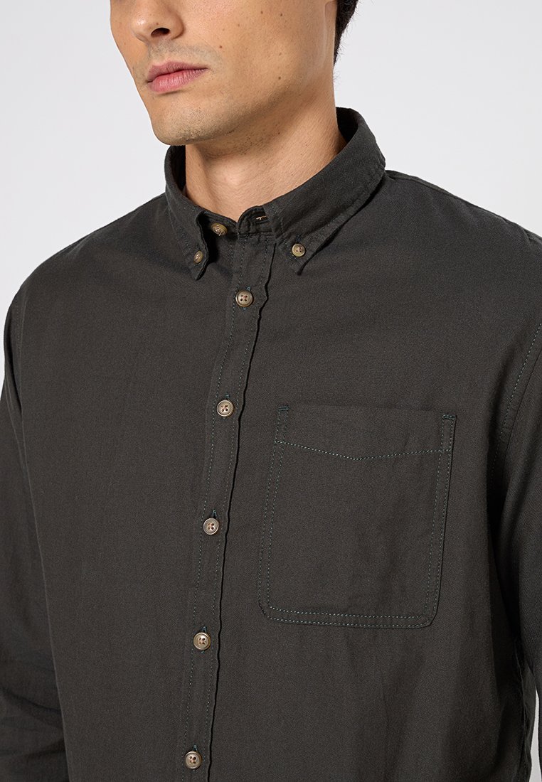 Camisa de botones verde oscuro en tejido de algodón, con cuello, bolsillo en el pecho con costuras en contraste y botones de color marrón claro.