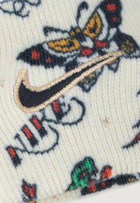 Tricotat dintr-un material crem, acest pulover prezintă modele de fluturi multicolori și are un logo Nike bordat în aur.