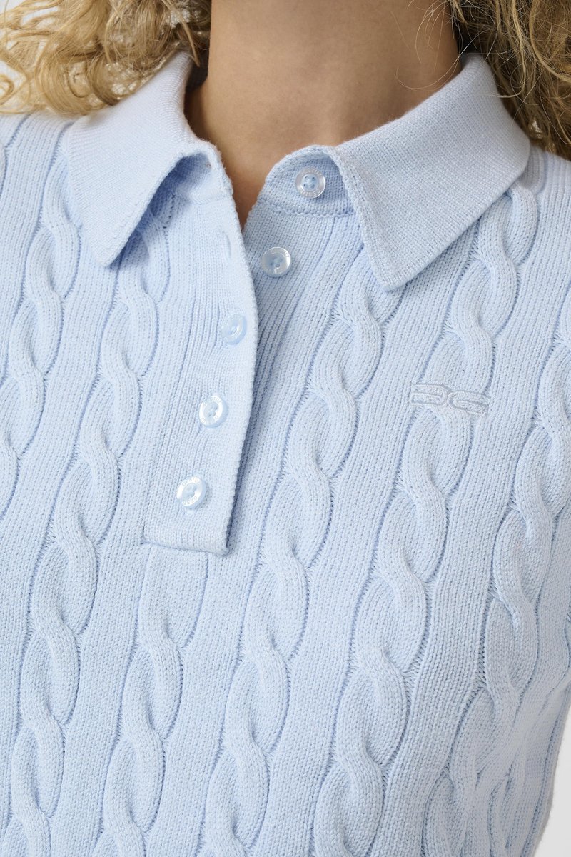 Pull polo bleu clair en maille torsadée avec quatre boutons et un col côtelé, porté par une personne aux cheveux blonds bouclés.