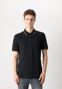 Tricou polo negru cu guler și marginile mânecilor contrastante de culoare bej, închidere cu trei nasturi și logo subtil al mărcii pe piept.