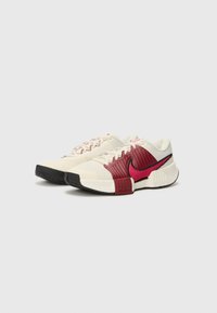 Nike athletic shoes featuring a cream upper, maroon ribbed accents, pink swoosh logo, black rubber sole, and textured material.