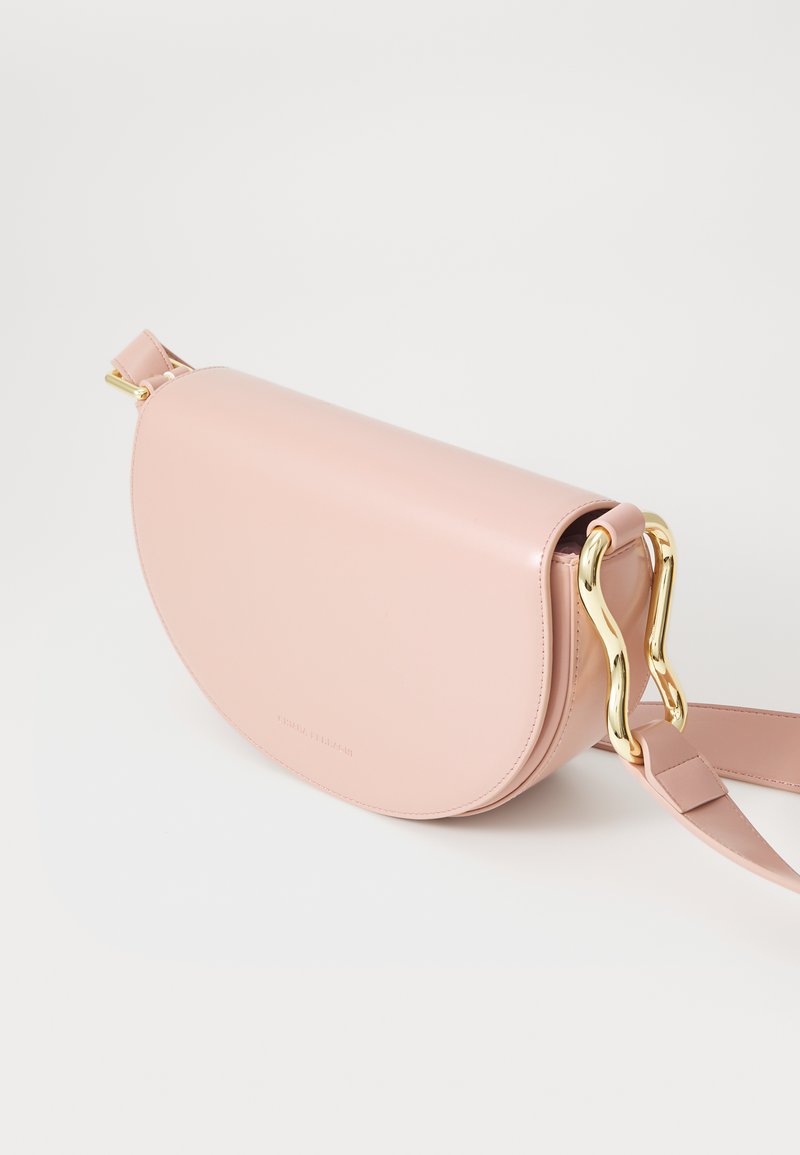 Rózsaszín bőr keresztpántos táska félhold alakban, arany színű fém kiegészítőkkel és levehető pánttal. Simább textúrával és minimalista dizájnnal rendelkezik.