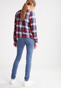 Röd och marinblå rutiga skjorta med långa ärmar, kombinerad med blå skinny jeans och vita sneakers. Skjortan har en avslappnad passform och ett klassiskt mönster.