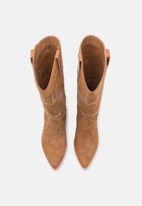 Botas de vaquero de ante marrón con puntas puntiagudas, diseños de costura intrincados y acentos de cuero en los bordes superiores. Dos tiradores para ponerlas y quitarlas fácilmente.